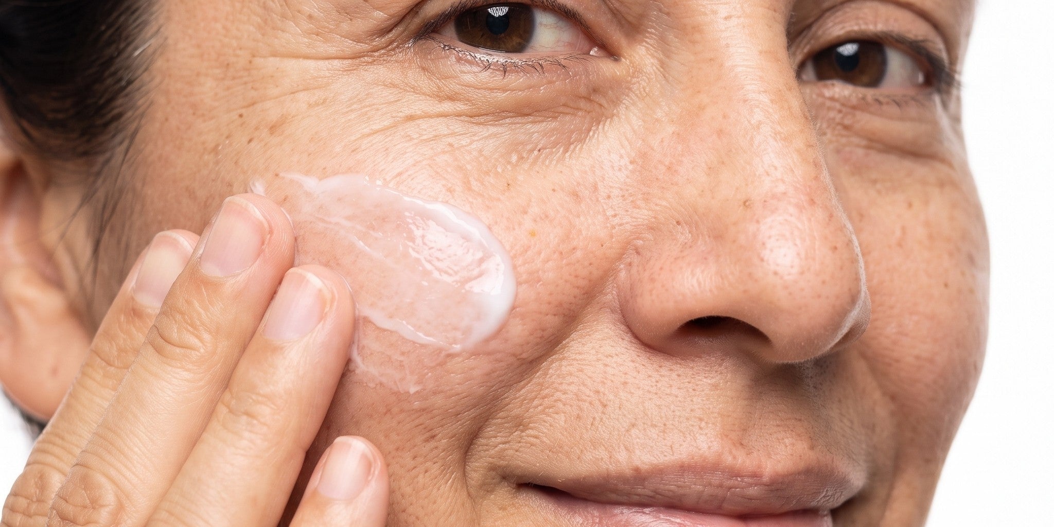 Mujer sonriendo aplicándose crema hidratante en la mejilla