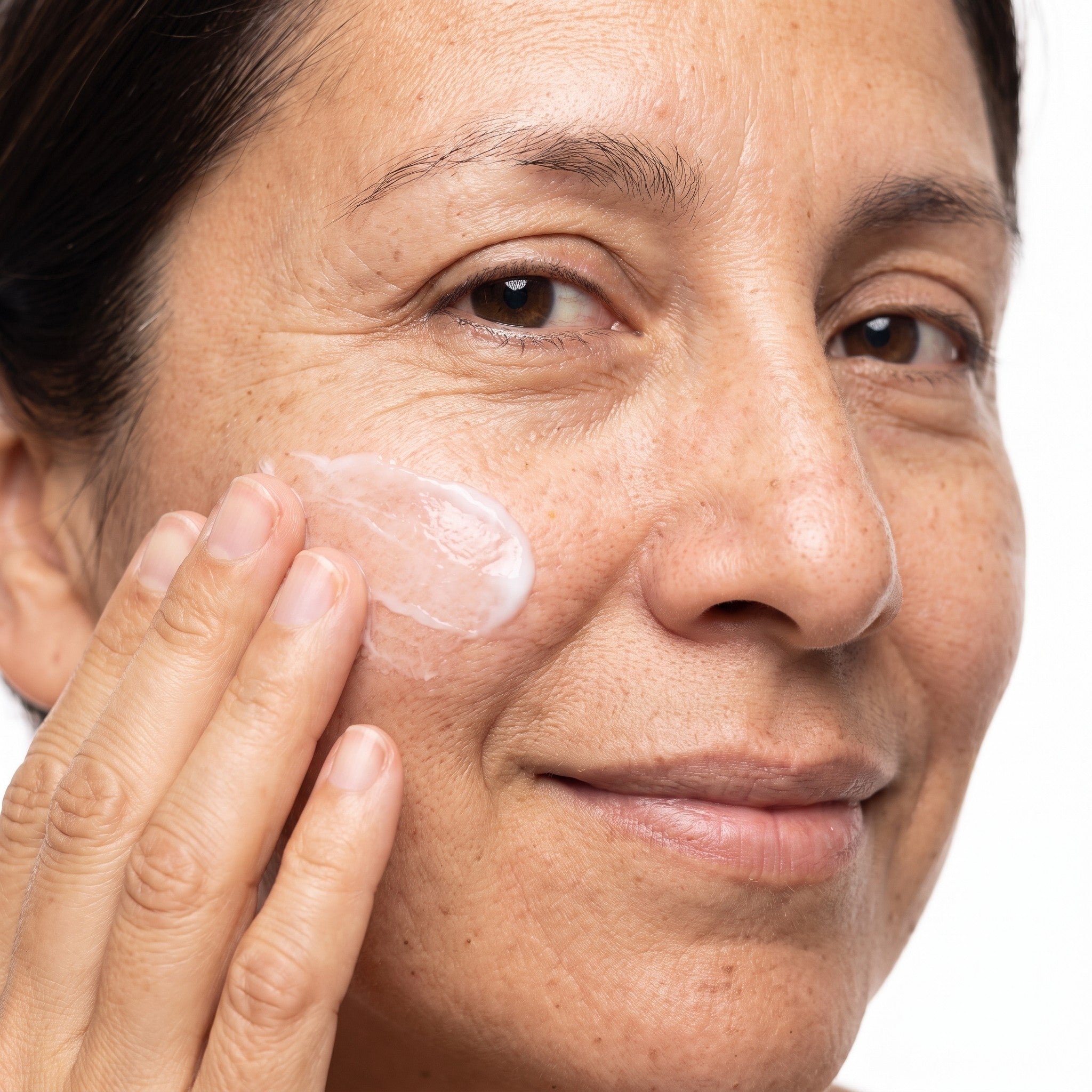 Mujer sonriendo aplicándose crema hidratante en la mejilla